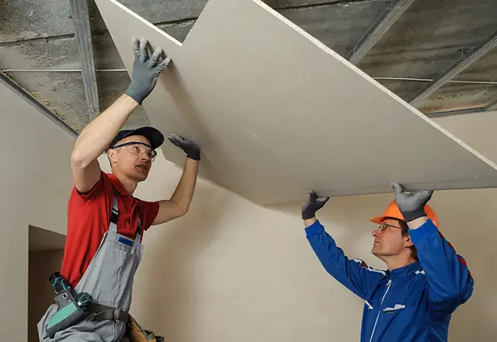 Two technicians lifting a drywall sheet into place