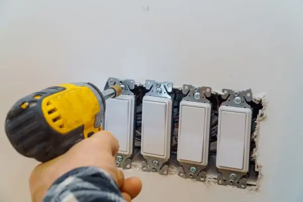 A technician installing new light switches with a drill